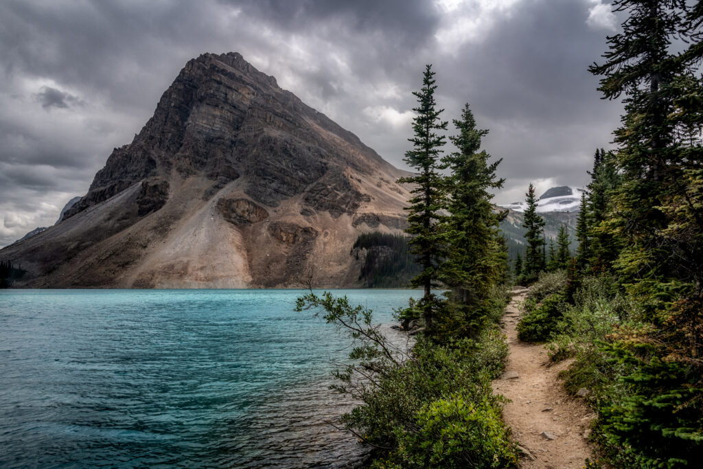 Dramatic mountain peak with turquoise lake and lush green trees under moody overcast sky wallpaper