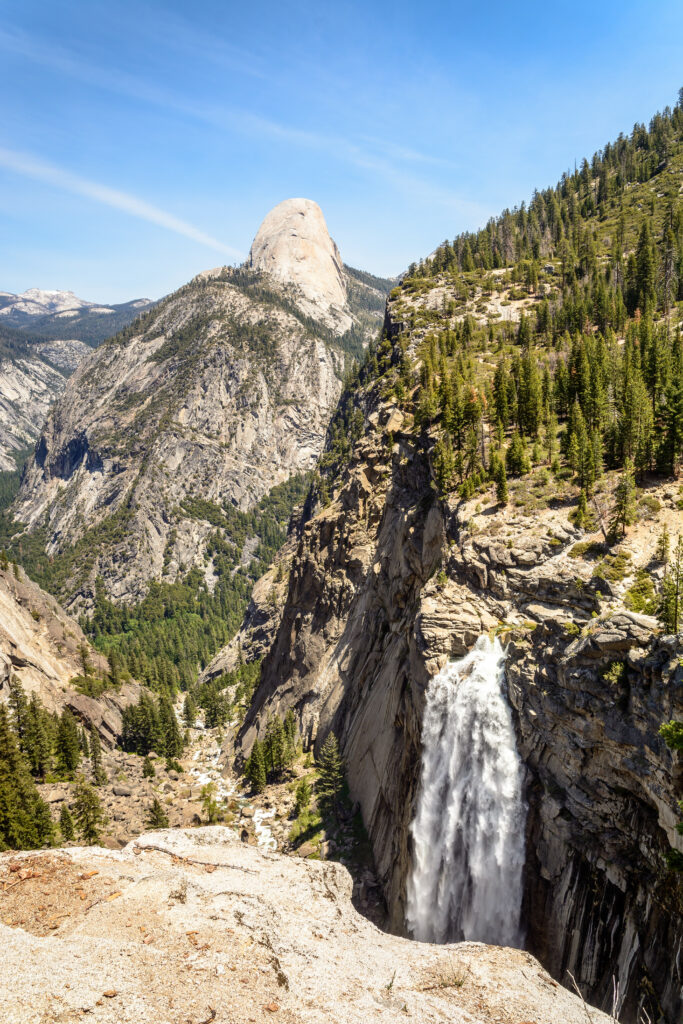 Dramatic mountain landscape with waterfall cliffs pine trees and clear blue sky wallpaper background