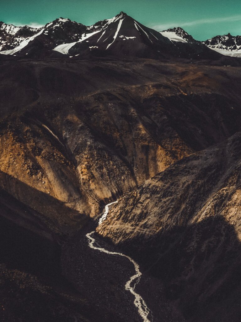 Winding river through rugged rocky terrain with snowcapped mountains dramatic landscape wallpaper