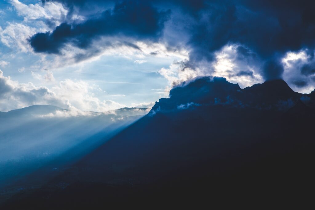 Dramatic mountain landscape with dark clouds fog and sunlight piercing shadowy foothills wallpaper
