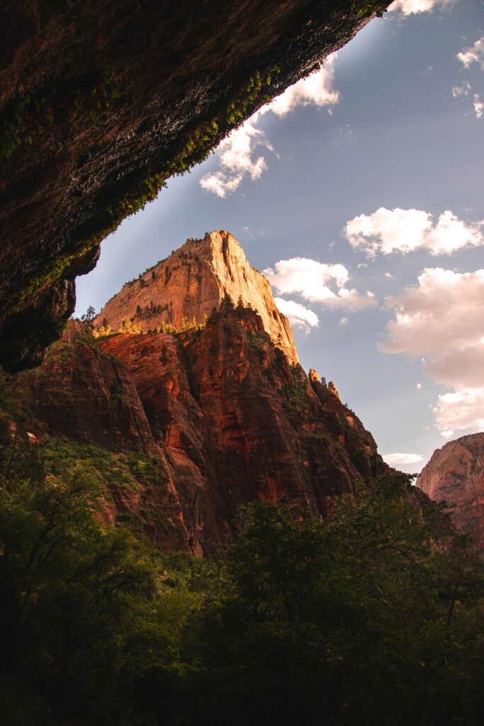 Dramatic rugged rock formations and towering mountains framed by cave shadow with green trees Wallpaper