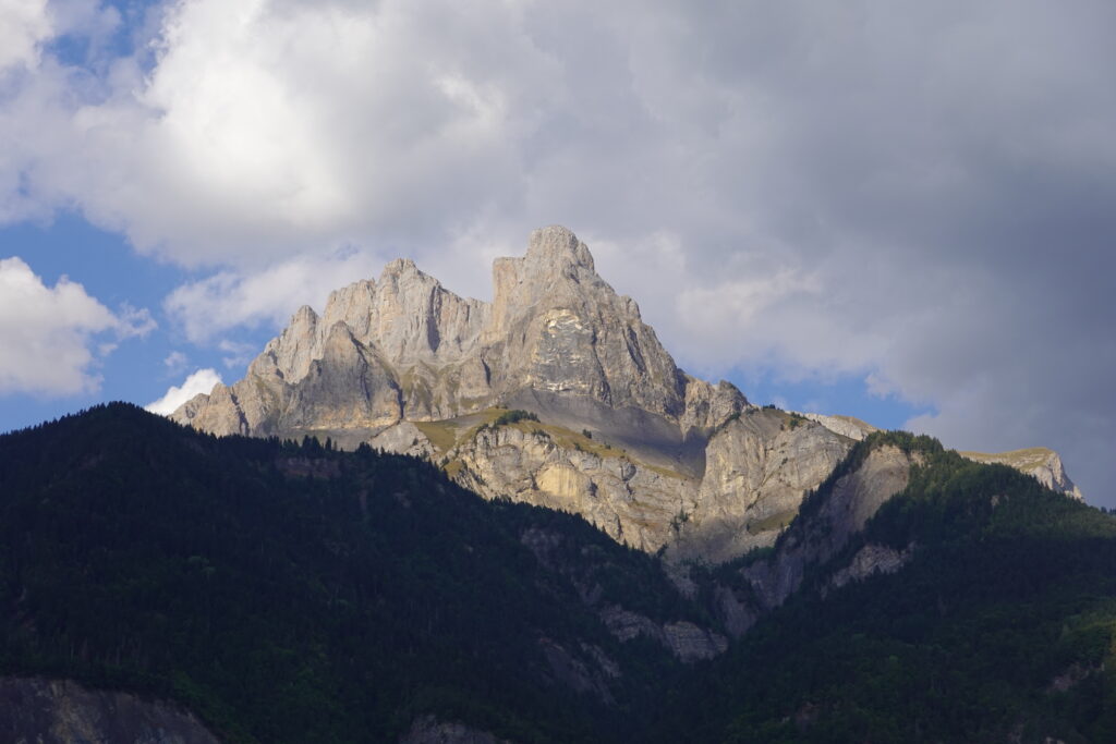 Dramatic mountain peak above green forest with sunlight and dynamic cloudy sky wallpaper background