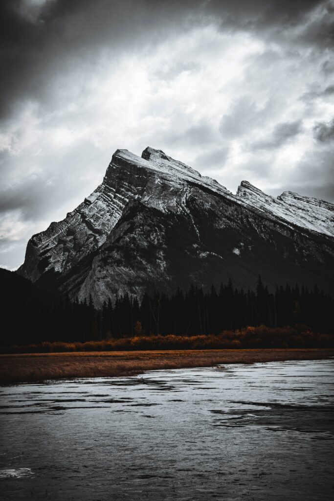 Dramatic mountain peak over rugged rocks and serene lake with moody clouds and earthy tones Wallpaper