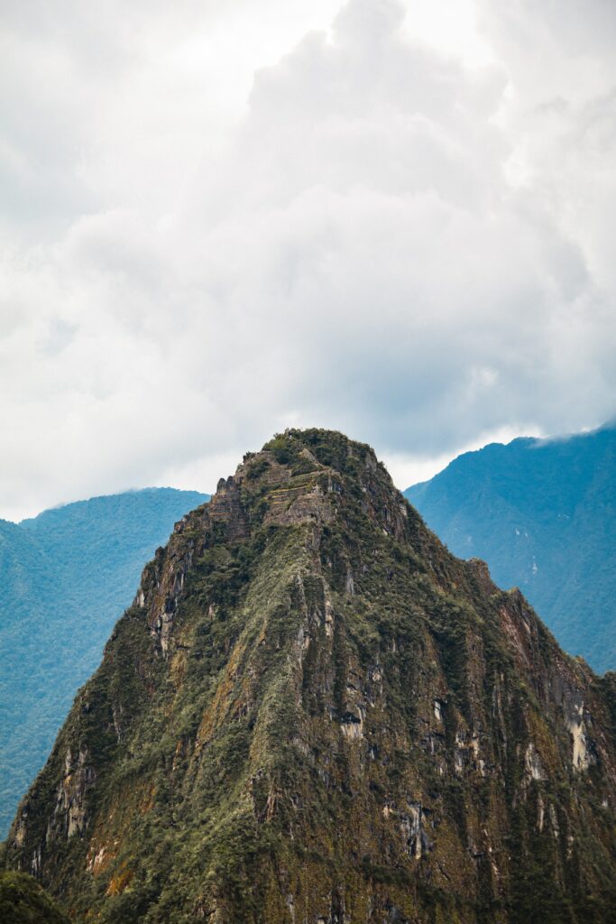 Dramatic mountain peak with rugged rocks lush greenery misty blue mountains and thick clouds wallpaper