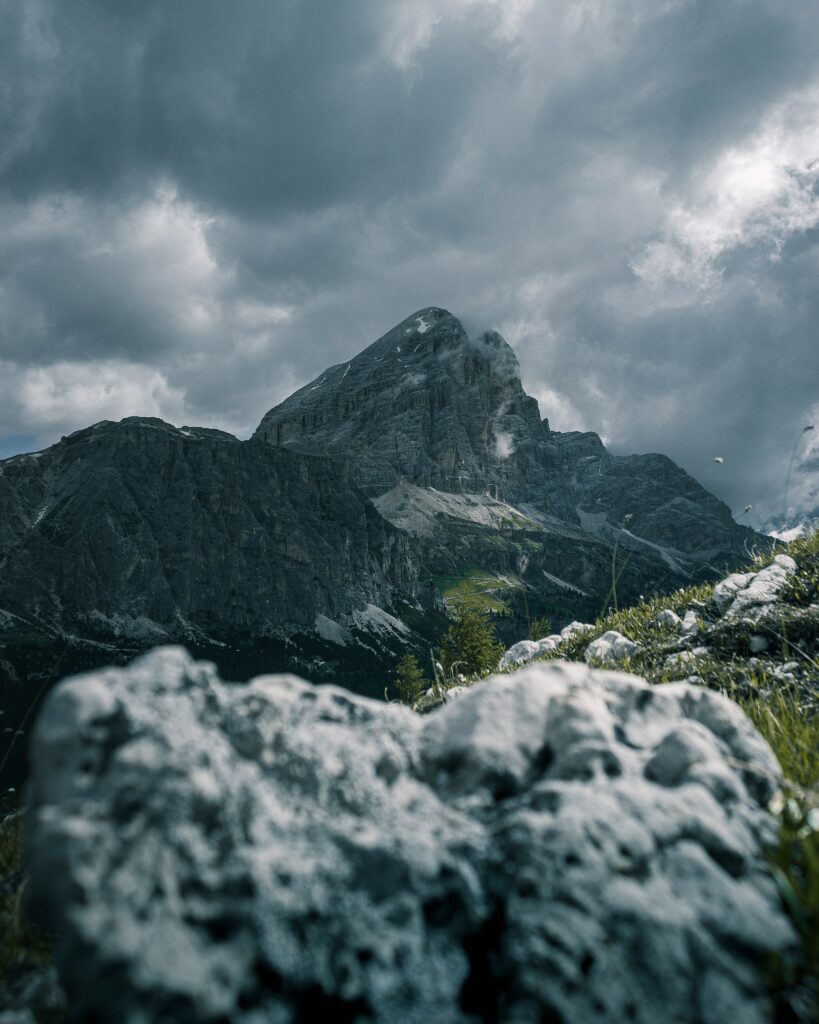 Dramatic mountain peak under moody sky with rugged rocks and lush greenery wallpaper background