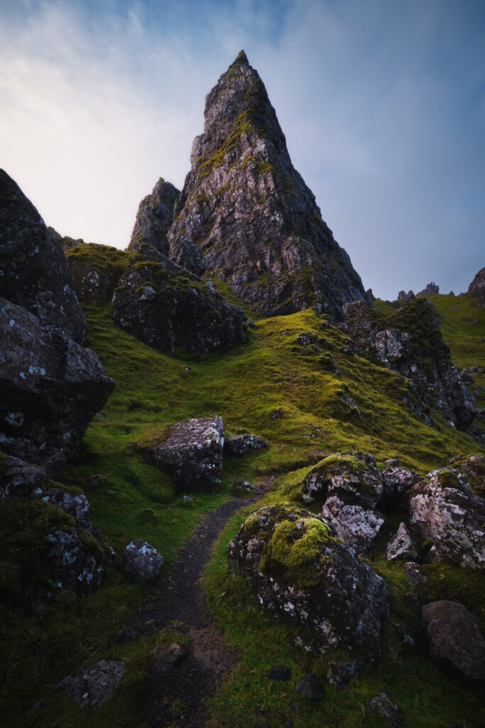 Dramatic mountain peak with rugged rocks lush green moss and stony path in cloudy sky background Wallpaper