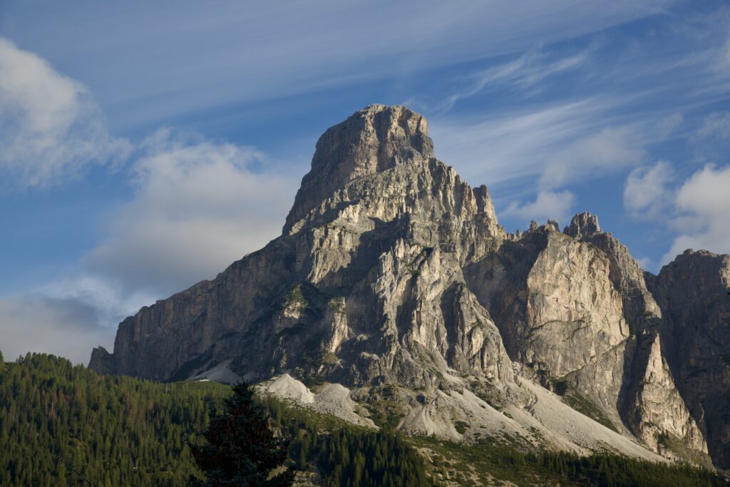 Dramatic mountain peak with rugged rocks and lush green forest under vivid blue sky wallpaper