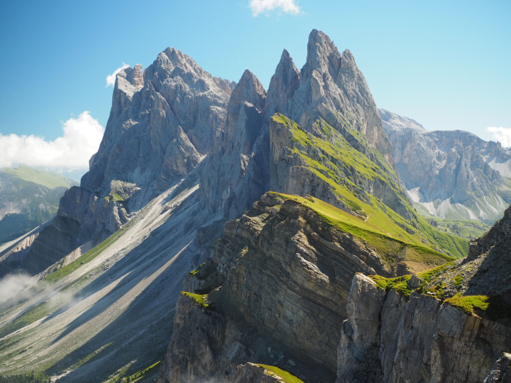 Rugged mountain peaks above green ridges and rocky slopes under a clear blue sky wallpaper
