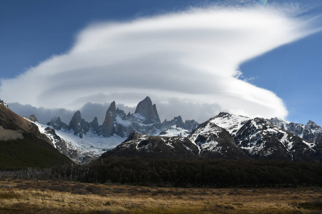 Dramatic mountain peaks with snow capped summits rugged rocks and trees under cloudy sky wallpaper