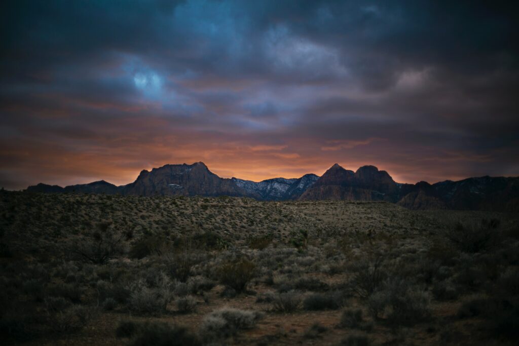 Sunset over rugged mountain peaks with rocky terrain and scattered bushes wallpaper background