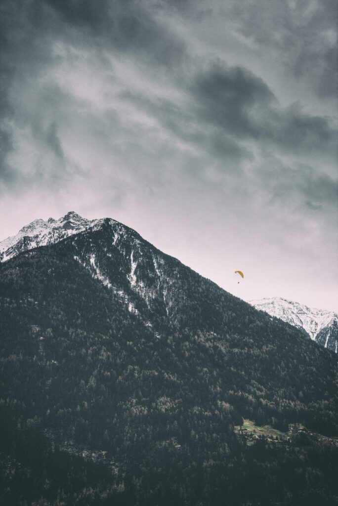 Dramatic mountain range with snow peaks and paraglider above dark forested slopes wallpaper