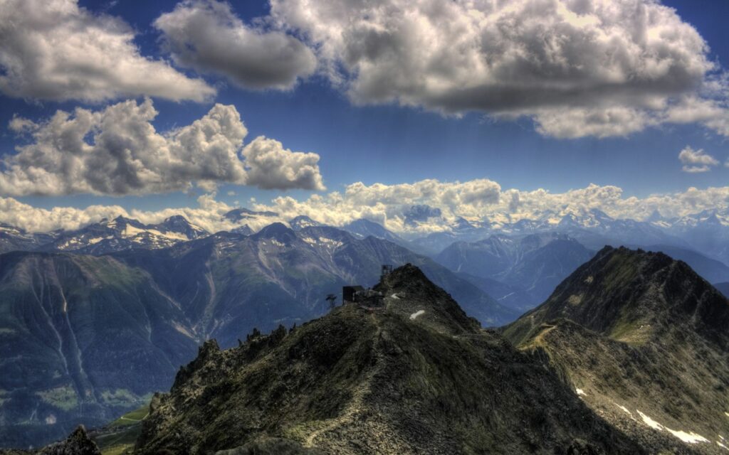 Dramatic mountain ridge under vivid blue sky with fluffy clouds and snow-capped peaks wallpaper