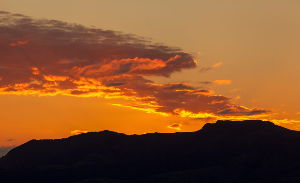 Mountain silhouette at sunset with fiery orange yellow and purple sky wallpaper background