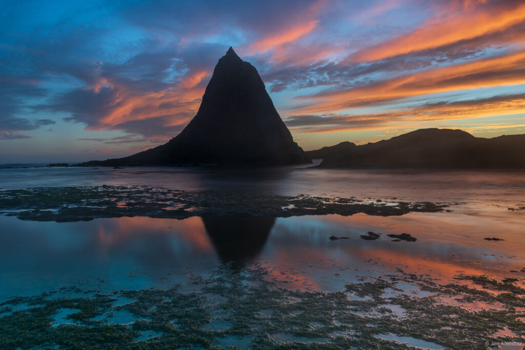 Dramatic mountain silhouette reflected in calm sea at vibrant orange and blue sunset wallpaper