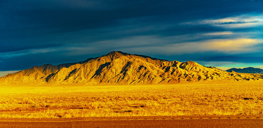 Dramatic mountain in golden desert under vivid sunset sky with rich yellows and deep blue clouds Wallpaper