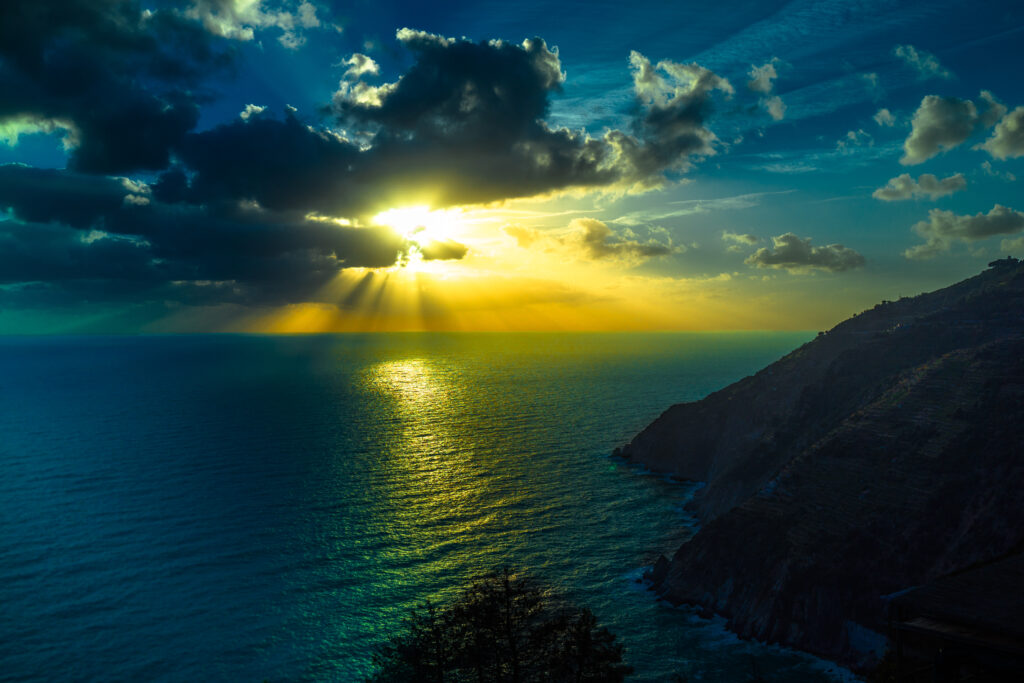 Dramatic sunset over mountains and ocean with golden light reflecting on shimmering sea wallpaper