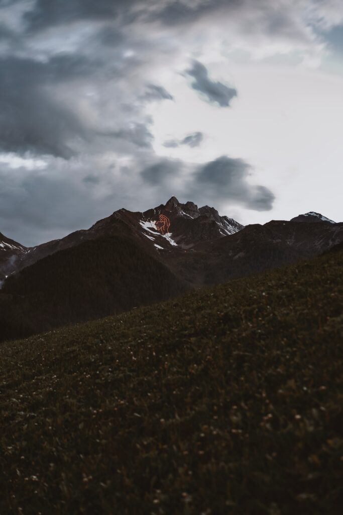 Dramatic alpine mountain wallpaper with rugged peaks grassy slopes and moody cloudy sky background