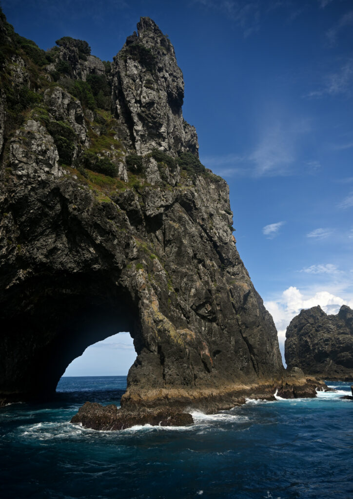 Natural rock arch over deep blue sea with rugged cliffs and crashing waves coastal landscape Wallpaper