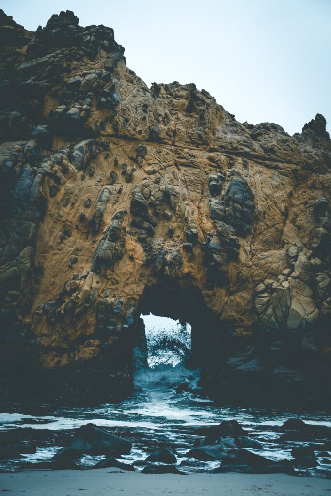Dramatic golden rock arch framing crashing sea and moody sky rugged coastal wallpaper background