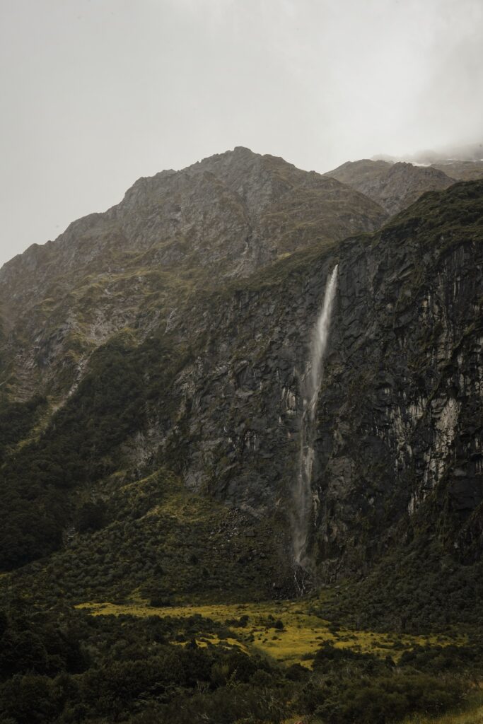 Dramatic New Zealand waterfall cascading rugged cliff in misty wild mountainous landscape wallpaper
