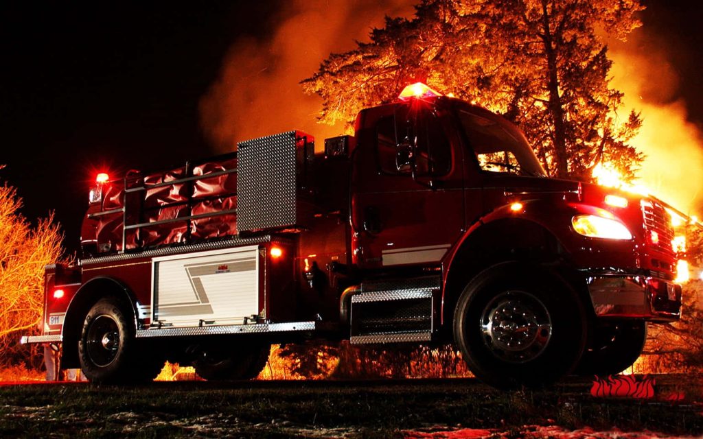 Night photo of red fire engine with flashing lights battling intense tree fire emergency Wallpaper
