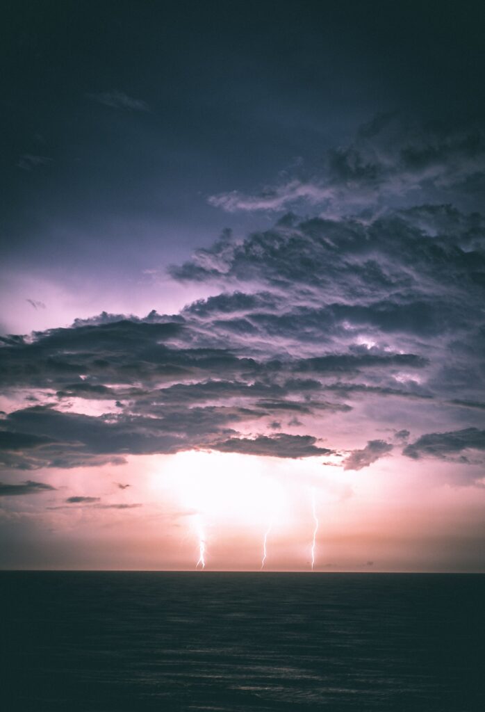 Dramatic night sea wallpaper with lightning bolts over cloudy purple pink sky at horizon