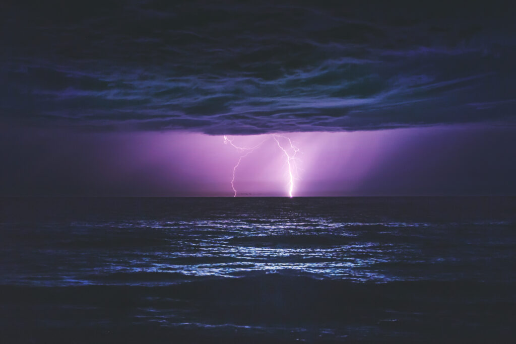 Dramatic night seascape with lightning illuminating dark clouds over tranquil ocean waves Wallpaper