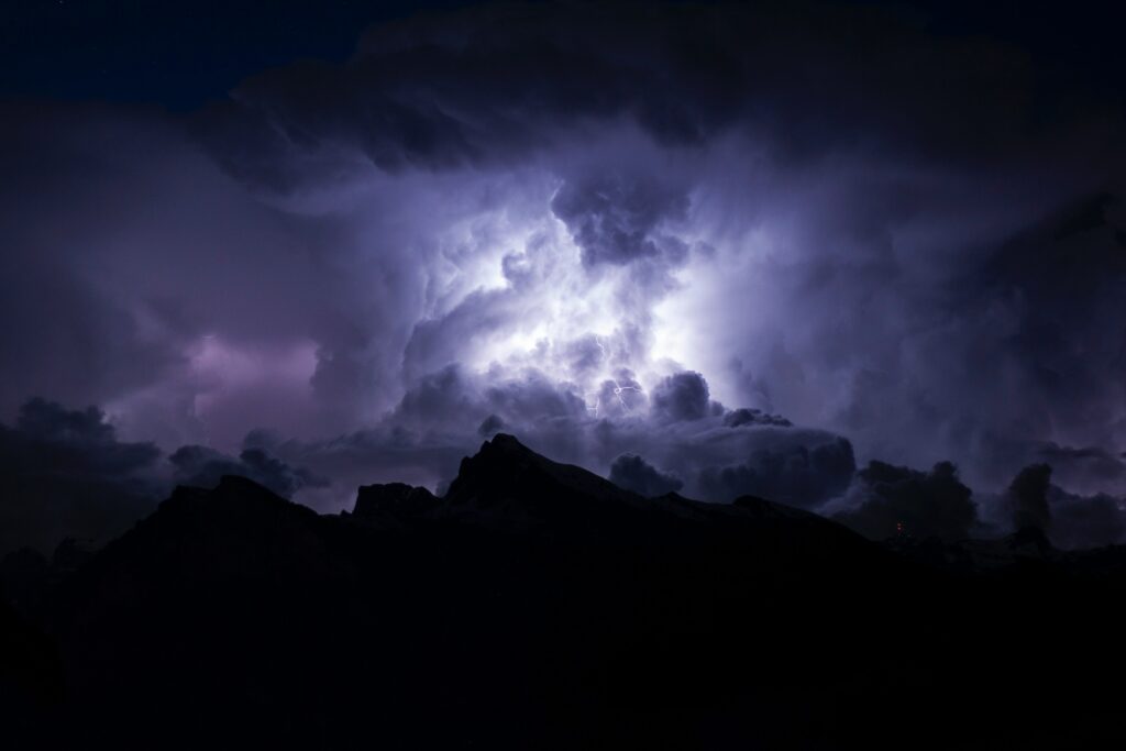 Dramatic night sky wallpaper with lightning over rugged mountain silhouette and dark storm clouds