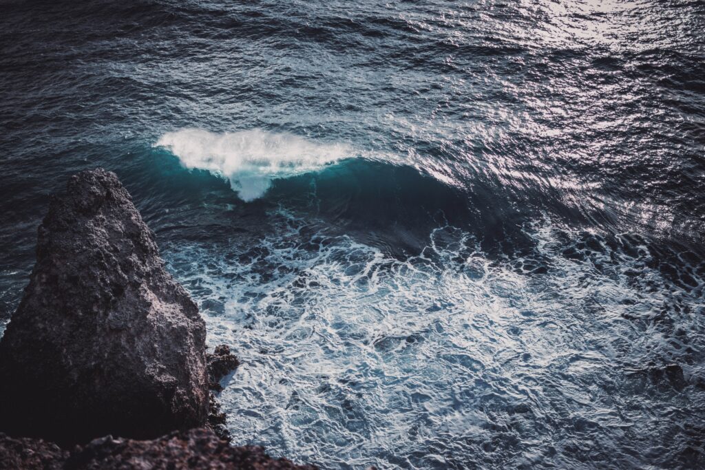 Powerful ocean wave crashing on rugged rock under bright sunlight in dramatic coastal scene Wallpaper