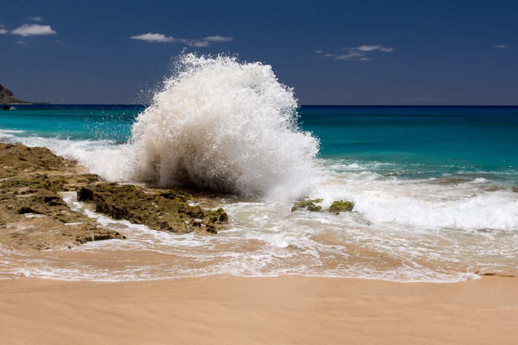 Dramatic wave crashes on rugged rocks with turquoise water and golden sand coastline wallpaper