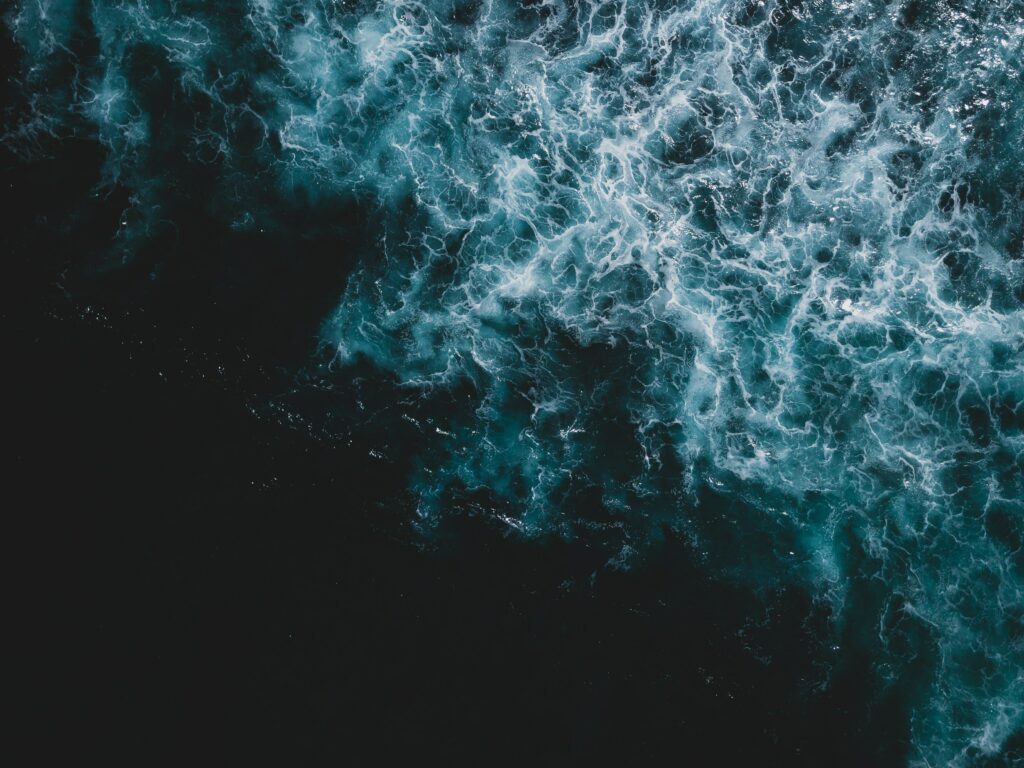 Aerial view of powerful ocean waves swirling dark blue waters with white frothy textures wallpaper
