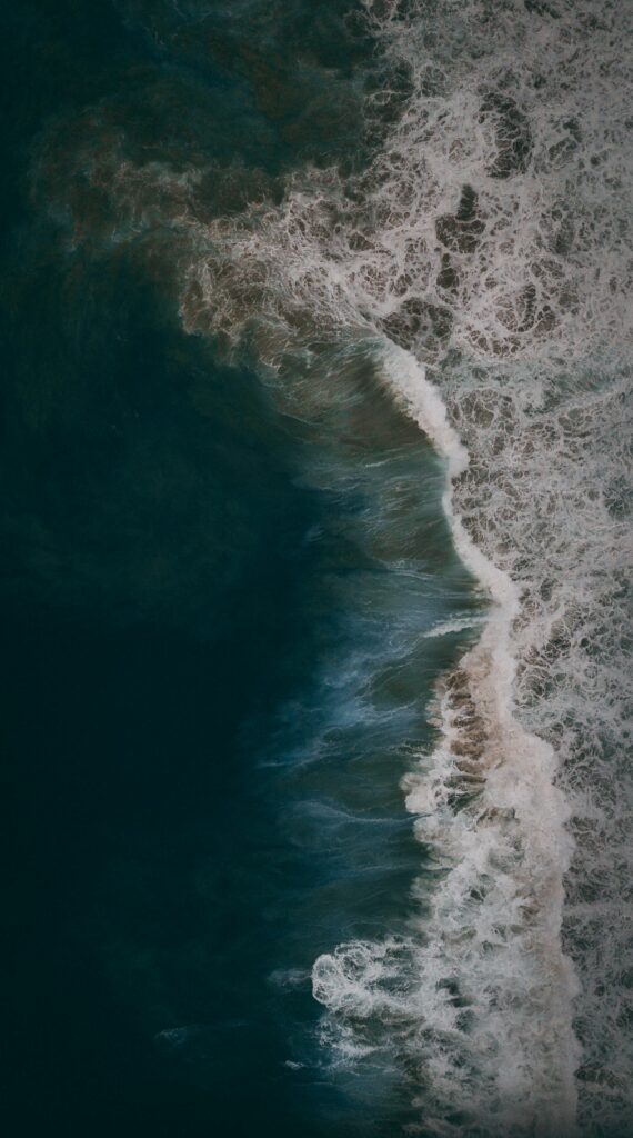 Aerial view of deep blue ocean waves crashing with white foam patterns natural wallpaper background