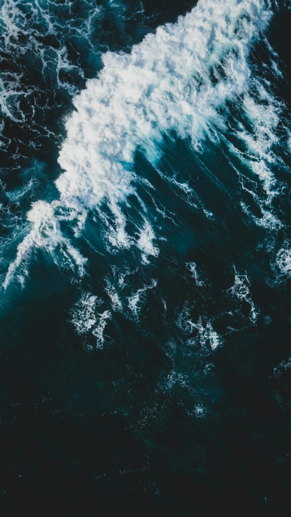 Aerial view of powerful ocean waves crashing with white foam on deep blue water for wallpaper