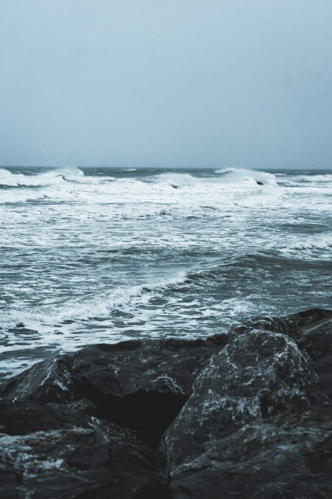 Dramatic ocean waves crashing on rugged rocks under moody gray overcast sky wallpaper background
