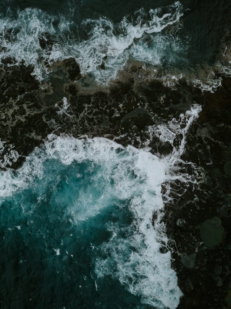 Aerial view of powerful sea waves crashing dark stones with white foam ocean wallpaper background