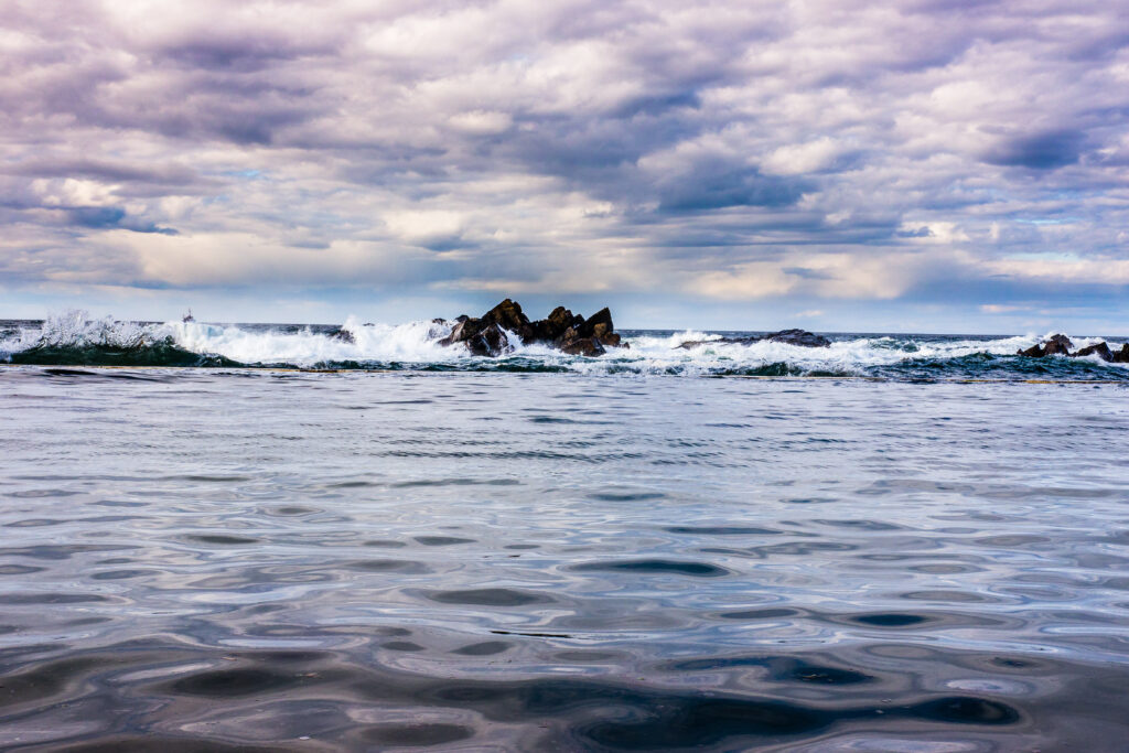 Powerful ocean waves crashing on rugged rocks under dramatic cloudy sky with deep blue tones Wallpaper