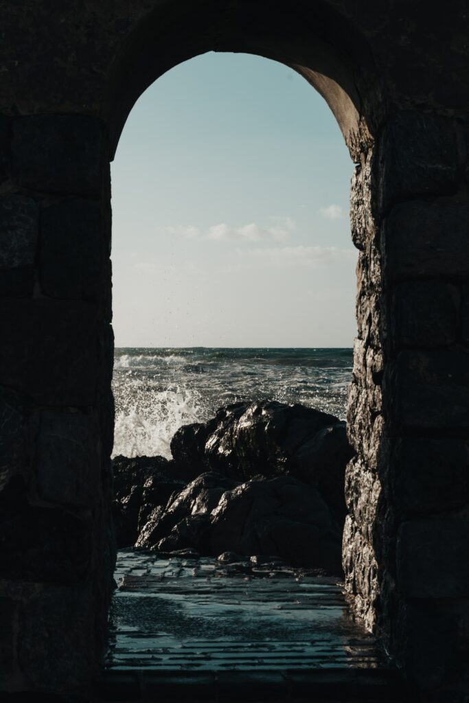 Dramatic sea view through stone archway with crashing waves and dark rocky shoreline wallpaper background