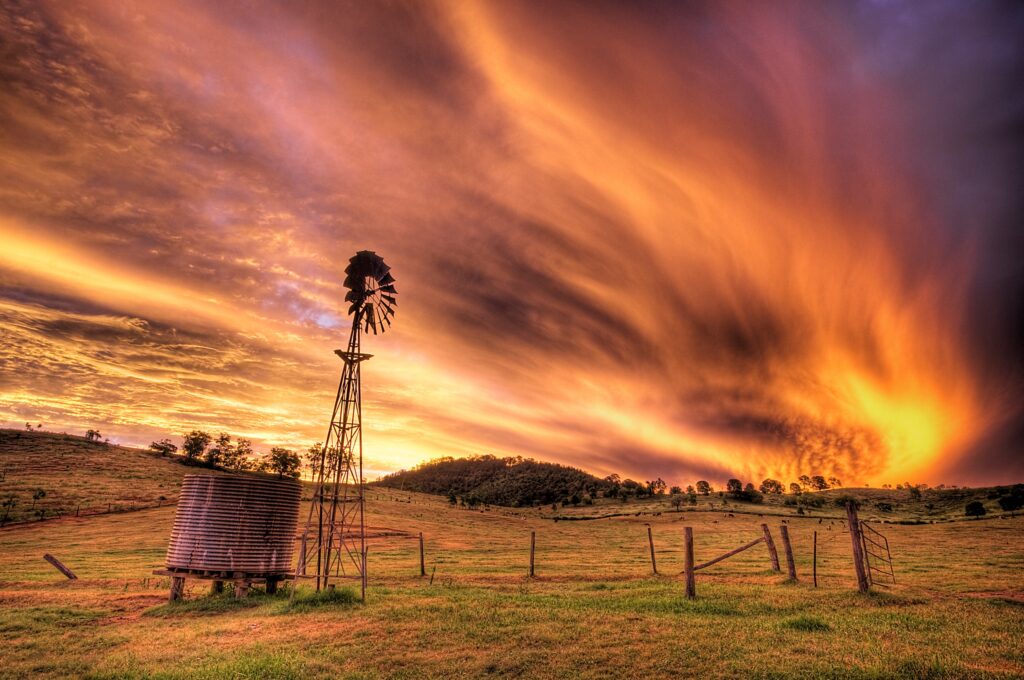 Dramatic sunset sky with orange purple clouds over rural field windmill and water tank wallpaper
