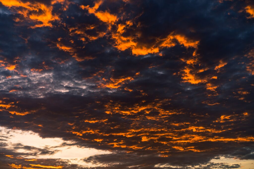 Dramatic sunset sky with vivid orange gold hues and dark overcast clouds wallpaper background