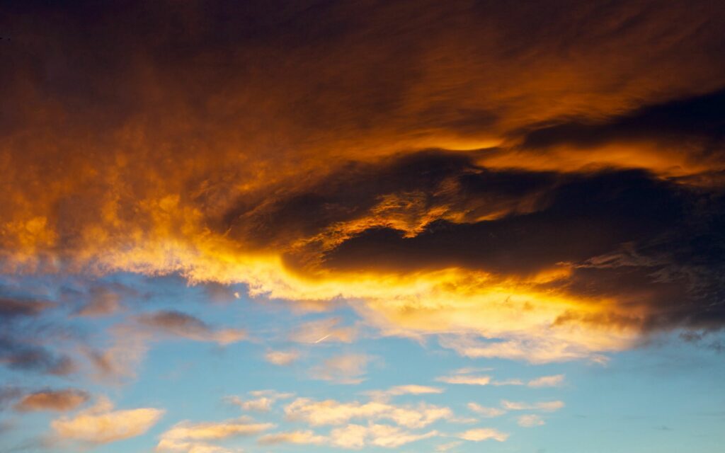 Dramatic orange and gray clouds blending over calm blue sky wallpaper background at sunset