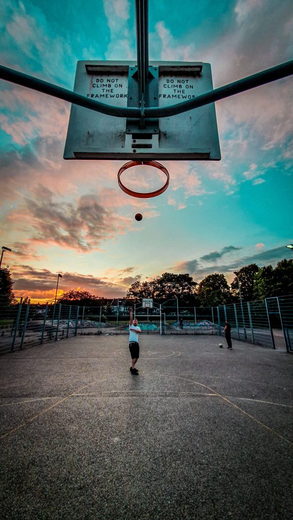 Basketball player shooting on outdoor court at sunset vibrant orange blue sky wallpaper background