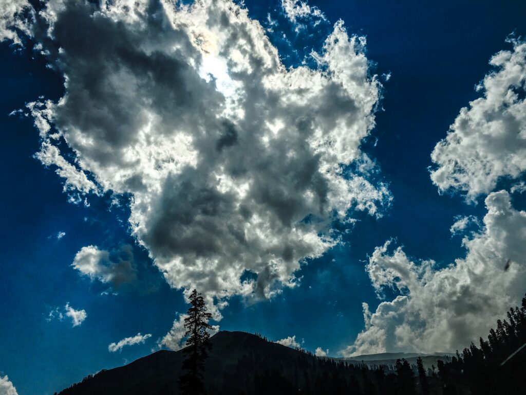 Dramatic overcast sky with sunlit billowing clouds over mountain silhouette wallpaper background