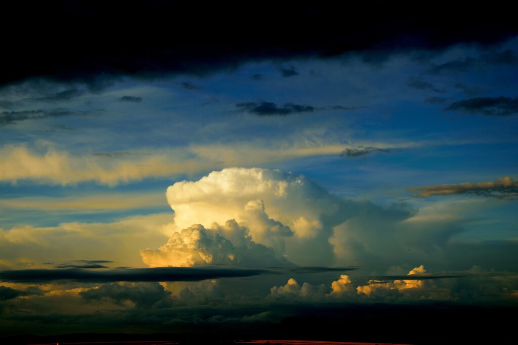 Dramatic overcast sky with towering sunlit cumulus clouds against deep blue and dark gray tones Wallpaper