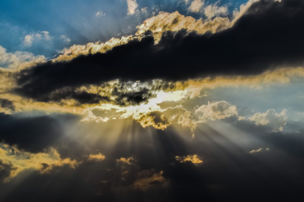 Dramatic sky with dark clouds and golden sunbeams breaking through natural wallpaper background
