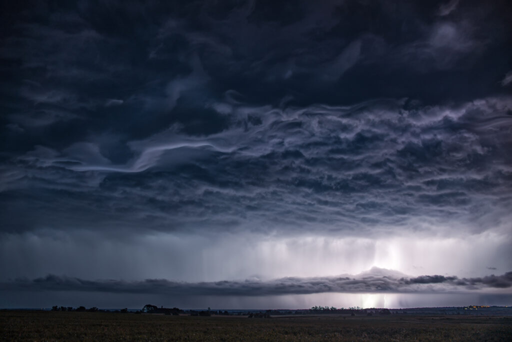 Stormy sky with dark swirling clouds and distant lightning over vast field dramatic weather wallpaper