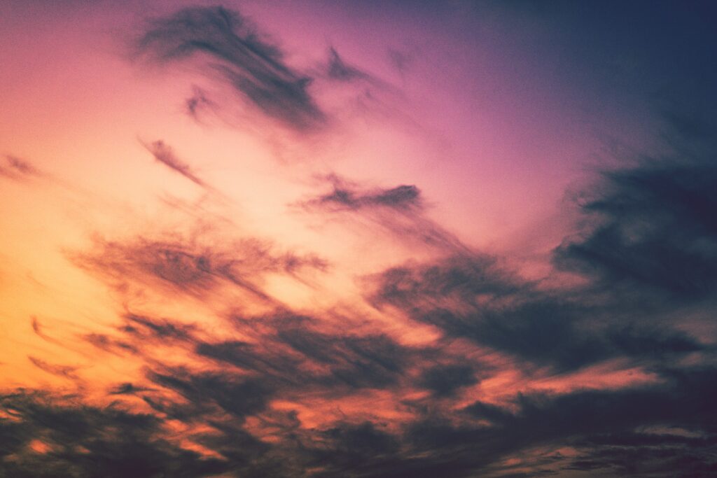 Dramatic porous clouds over vibrant sunset sky with warm orange gold and purple pink hues wallpaper