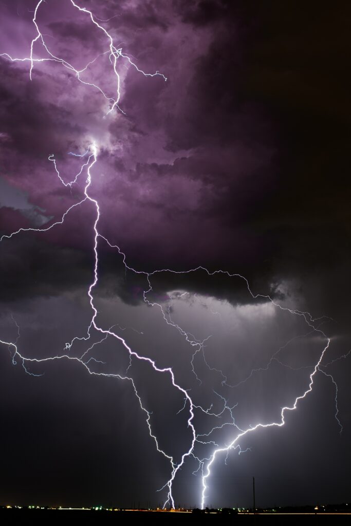 Dramatic purple lightning bolts crackle across a stormy sky over a dark distant landscape wallpaper