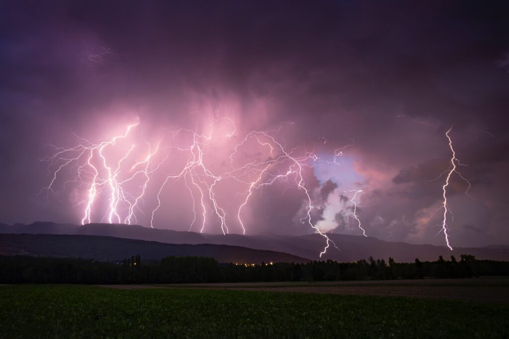 Dramatic lightning bolts illuminate purple stormy sky over peaceful horizon thunderstorm wallpaper
