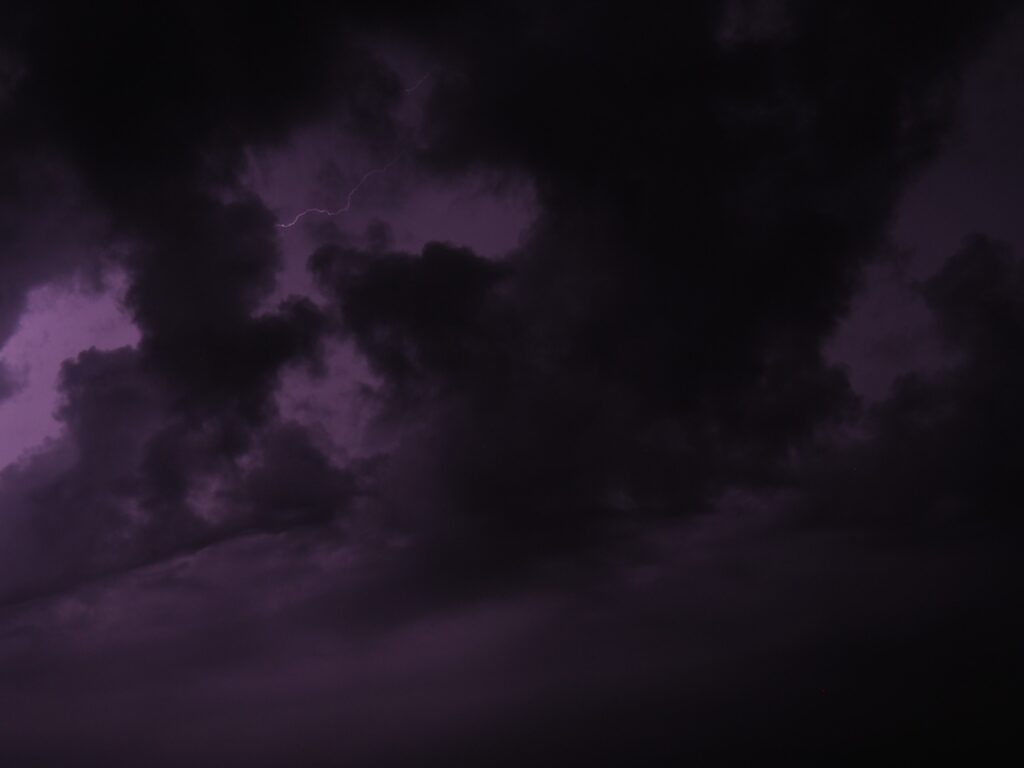 Dramatic storm clouds with purple lightning showcasing intense thunderstorm power wallpaper background