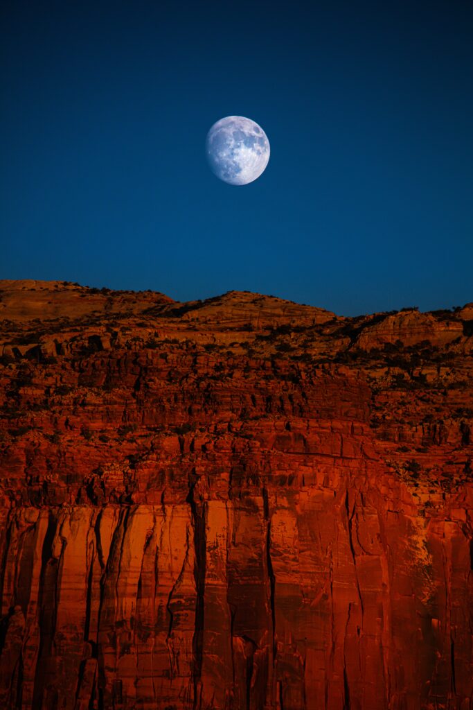 Rugged red cliffs and rocky canyon under bright detailed moon and deep blue sky wallpaper background